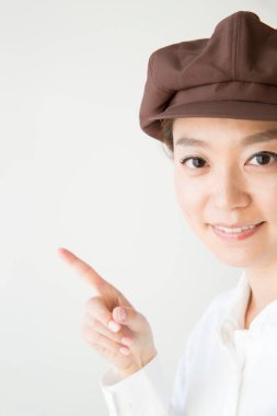 Şapkalı genç Asyalı kadın beyaz arka planı işaret ediyor. 