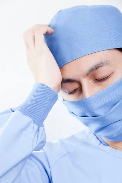 asian surgeon wearing blue uniform suffering from headache