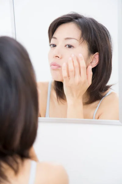 woman looking at mirror and applying cream