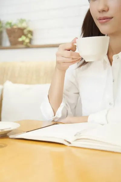 woman holding cup of coffee and reading book  at home