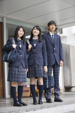 Aynı üniformayı giyen bir grup öğrenci okullarında birlikte dikiliyorlar.