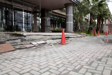 Çağdaş binanın yanında turuncu güvenlik konileri olan hasarlı kaldırım.