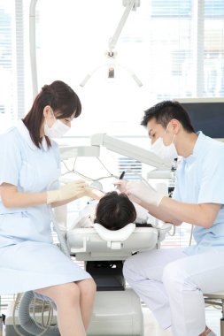 Asyalı erkek ve kadın dişçiler hastanın ağzını inceliyor.