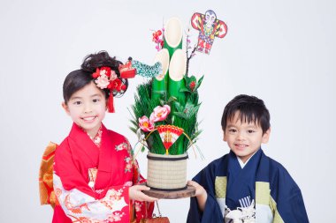 Kimono giyen gülümseyen çocuklar ellerinde şenlikli kadomatsu düzeneği tutuyorlar.
