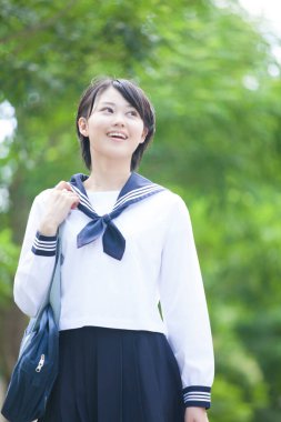 gülümseyen Japon kız öğrenci üniformalı parkta poz veriyor.