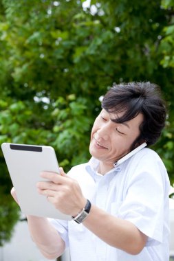 Adam parkta dijital tablet ve akıllı telefon kullanıyor 