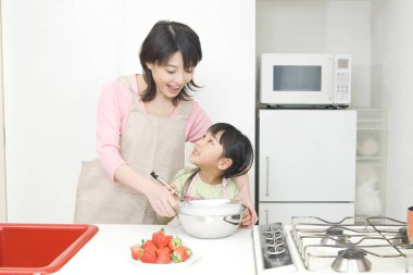 Gülümseyen Japon kadın ve kızı mutfakta yemek pişiriyor.