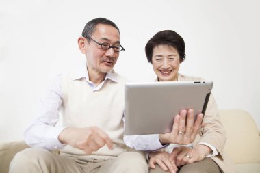 Asyalı yaşlı çift evde tablet kullanıyor. 