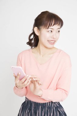 Pembe kazaklı genç Japon kadının beyaz arka planda telefon kullanarak stüdyo portresi. 