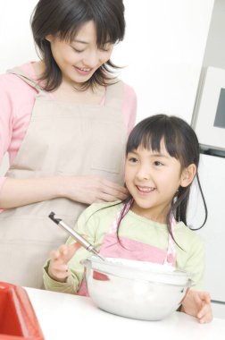 Gülümseyen Japon kadın ve kızı mutfakta yemek pişiriyor.