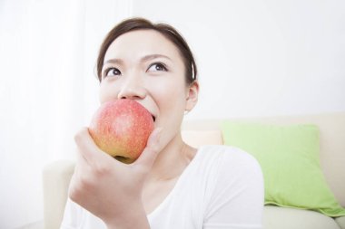 Genç Asyalı kadın evde elma yiyor. 