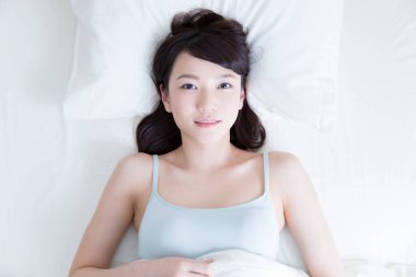 Genç Asyalı kadın yatakta yatıyor.
