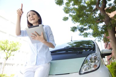 Kadın arabanın yanında dururken dijital tabletini kullanıyor. 