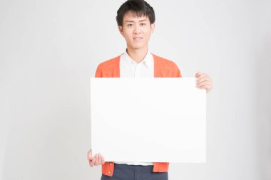 Sıradan giyinmiş genç Asyalı adam beyaz arka planda beyaz boş bir pankart tutuyor..