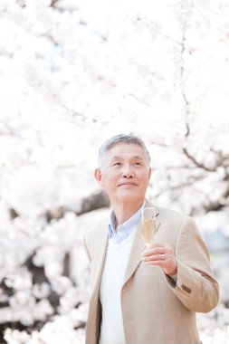 Beyaz gömlekli son sınıf öğrencisi parkta şampanya bardağı tutuyor. 