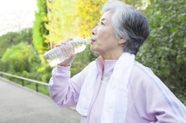 Yaşlı Asyalı kadın su içiyor.