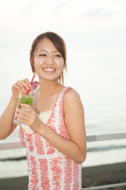 Asyalı kız sahilde kokteyl içiyor. 