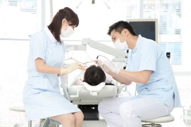 Asyalı erkek ve kadın dişçiler hastanın ağzını inceliyor.