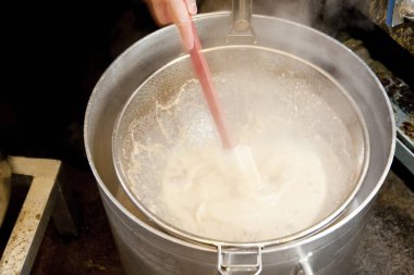 Büyük metal tencerenin içinde kalın sıvı karıştırır.