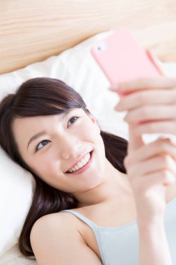 Kadın yatak odasında akıllı telefonuyla selfie çekiyor.