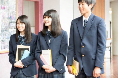 Aynı üniformayı giyen bir grup öğrenci okullarında birlikte dikiliyorlar.