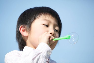 Tatlı Asyalı çocuk mavi gökyüzüne karşı sabun köpükleri üflüyor.