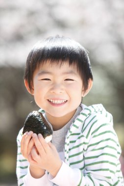 Asyalı küçük çocuk dışarıda bir şeyler yiyor.