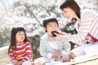 Asyalı anne kız ve oğlu parkta piknik yapıyorlar.