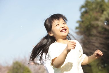 Mutlu Asyalı küçük kız parkta sabun köpüğüyle oynuyor.