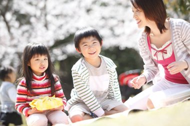 Asyalı anne kız ve oğlu parkta piknik yapıyorlar.