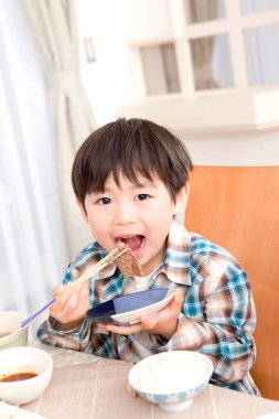 Asyalı küçük çocuk mutfakta et yiyor.