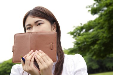 Parkta elinde defter tutan genç bir kadın.