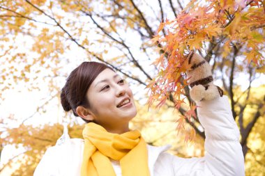 Parkta sonbahar yaprakları olan genç Japon kadın.