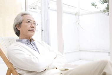 Yaşlı Asyalı adam evde dinleniyor ve düşünüyor. 