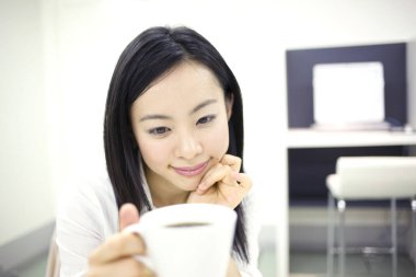 Genç Asyalı kadın bir fincan kahve içiyor.
