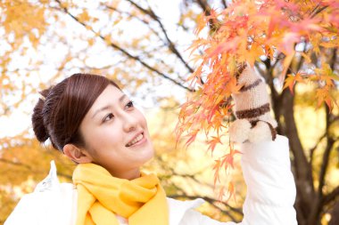 Parkta sonbahar yaprakları olan genç Japon kadın.