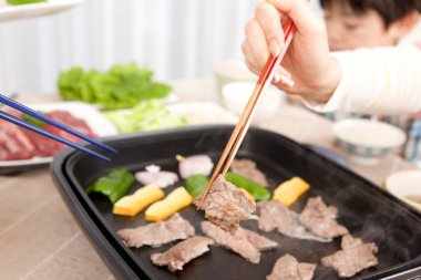 İnsanlar masada et ve sebze pişiriyor.