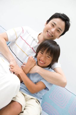 Gülümseyen adam kanepede neşeli çocuğa sarılıyor.