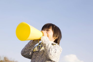Gökyüzünün altında sarı megafon kullanan çocuk