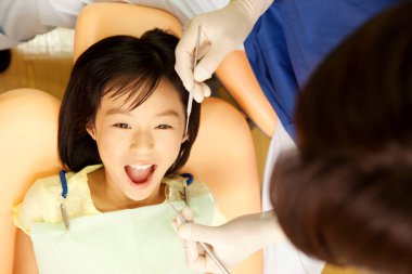 Dişçi, dişçi koltuğunda kızların dişlerini muayene ediyor. 