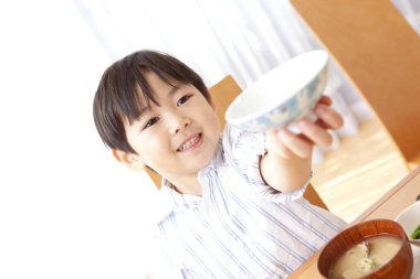 Gülümseyen çocuk masada kaseyi tutuyor.