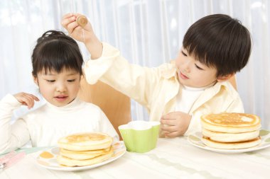 Küçük tatlı Asyalı çocuk ve kız mutfakta krep yiyorlar. 