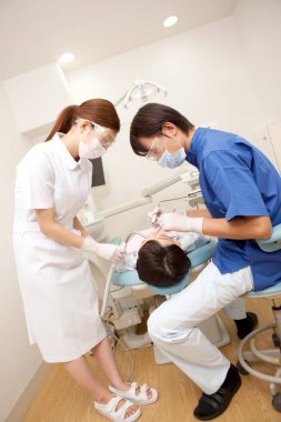Üniformalı kadın ve erkek dişçiler hastasıyla çalışıyor.