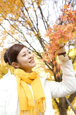 Parkta sonbahar yaprakları olan genç Japon kadın.