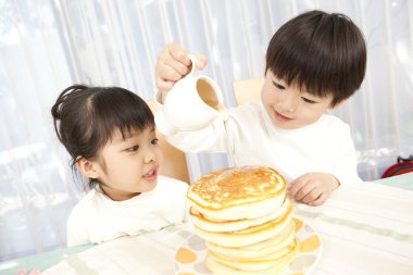 Küçük tatlı Asyalı çocuk ve kız mutfakta krep yiyorlar. 