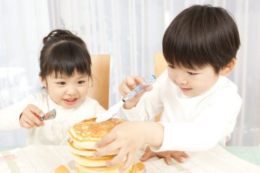 Küçük tatlı Asyalı çocuk ve kız mutfakta krep yiyorlar. 