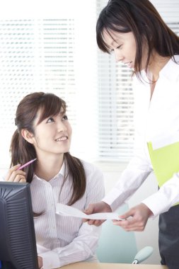 İki Asyalı iş kadını modern bir ofiste bir şey tartışıyor.