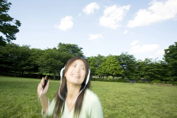 在夏季公园里 年轻的亚洲女人在耳机里听音乐 — 图库照片