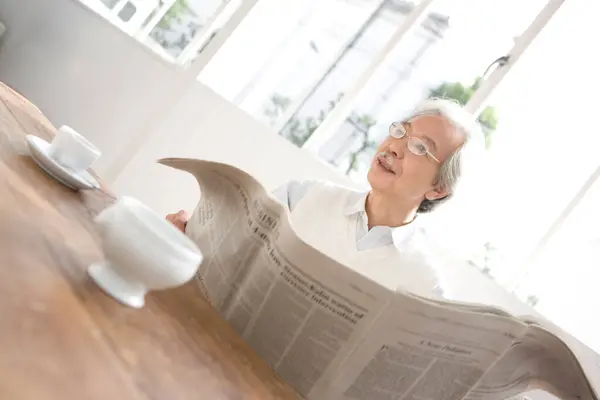 senior man with newspaper sitting at table