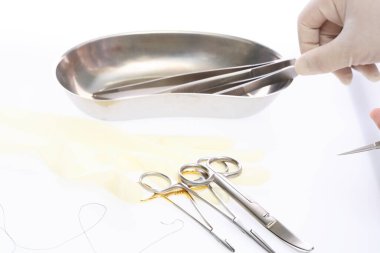 Eldivenli el, ameliyat aletlerinin yanında, böbrek tepsisinin üzerinde forseps tutuyor.